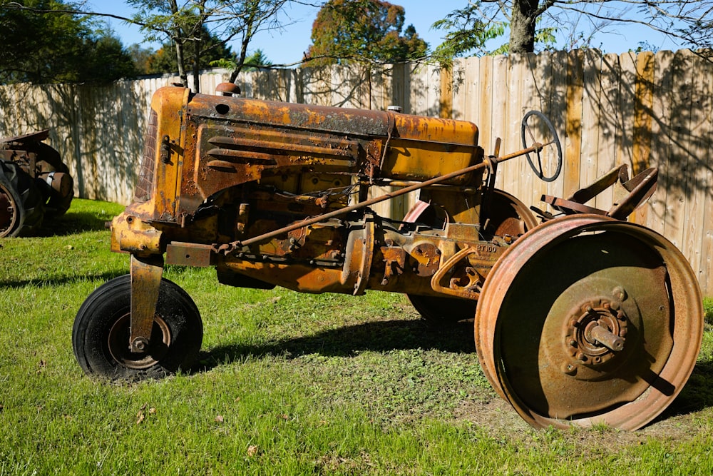 an old tractor sitting in the grass next to a fence