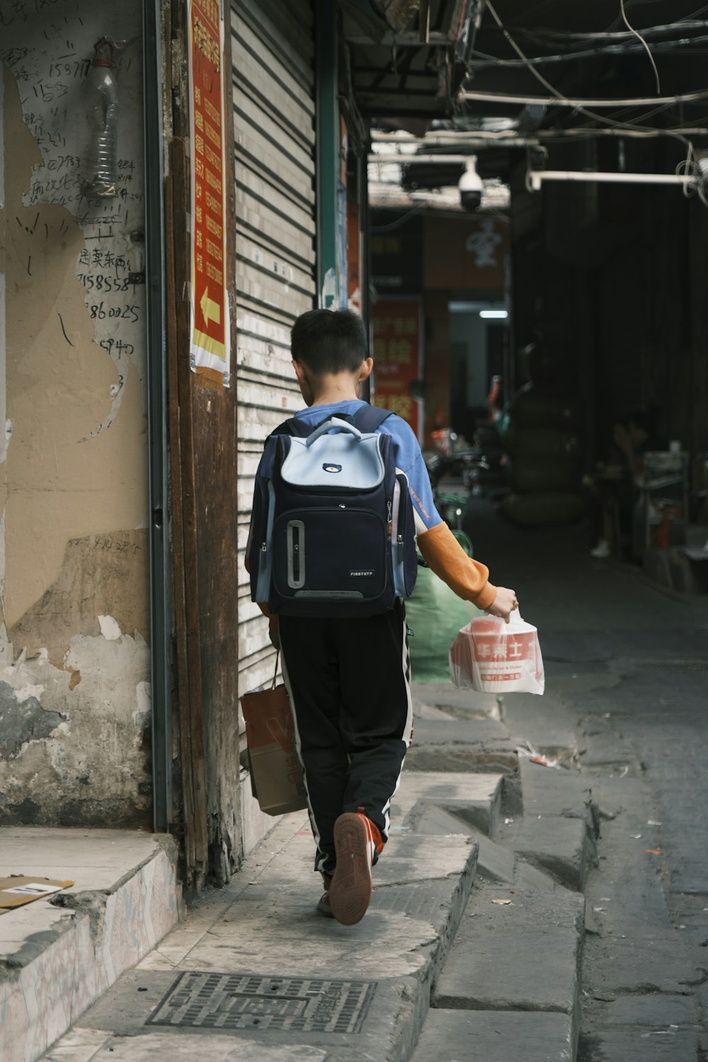 a young boy walking down a street carrying a backpack