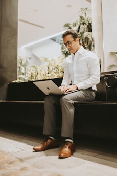 A focused white American professional in business casual attire working on a laptop in a modern office setting with dark blue and black accents.
