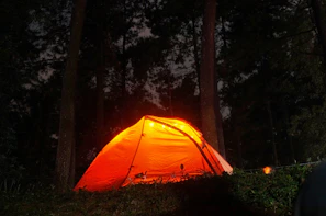 A cozy camping tent illuminated by warm lantern light at dusk in a forest clearing