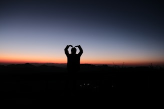 Sunset silhouette of an athlete wearing Titansportz gear, standing tall on a mountain peak.