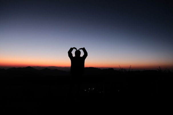 Sunset silhouette of an athlete wearing Titansportz gear, standing tall on a mountain peak.