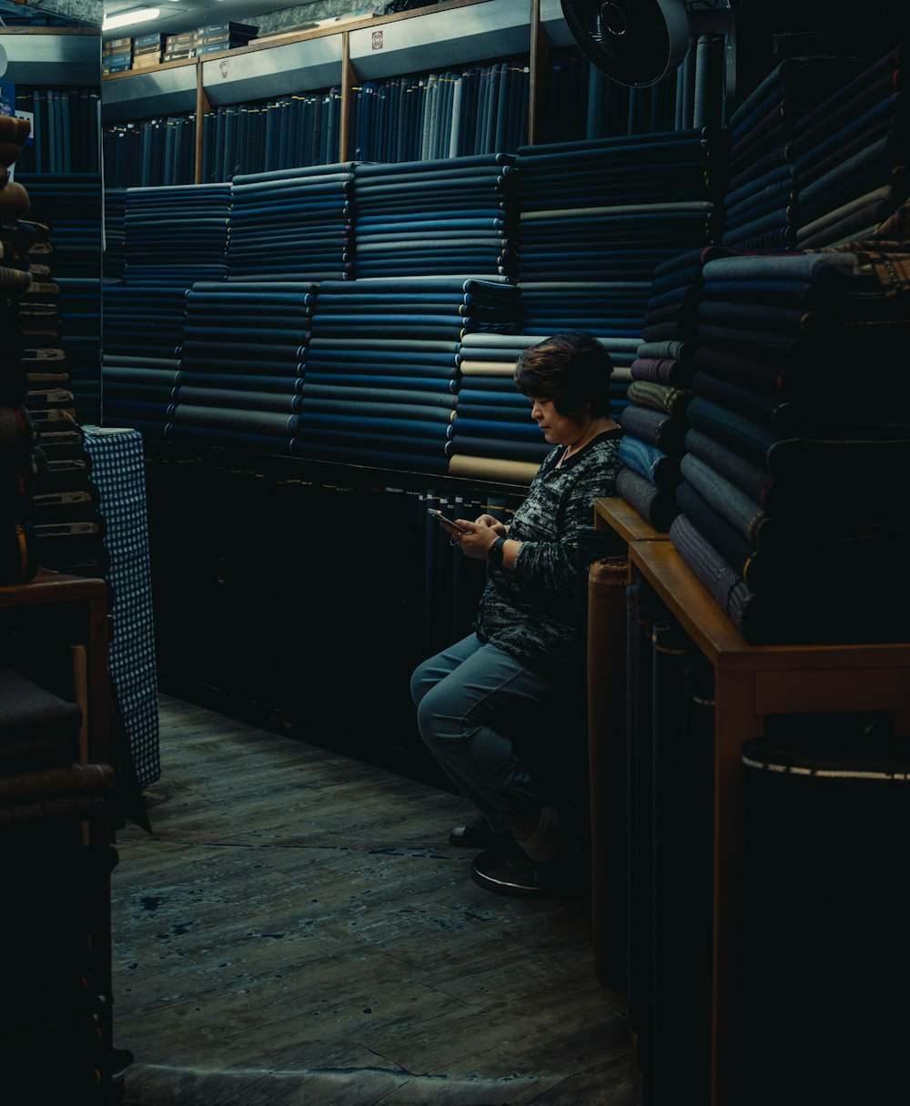 a man sitting on a chair in a room filled with stacks of books