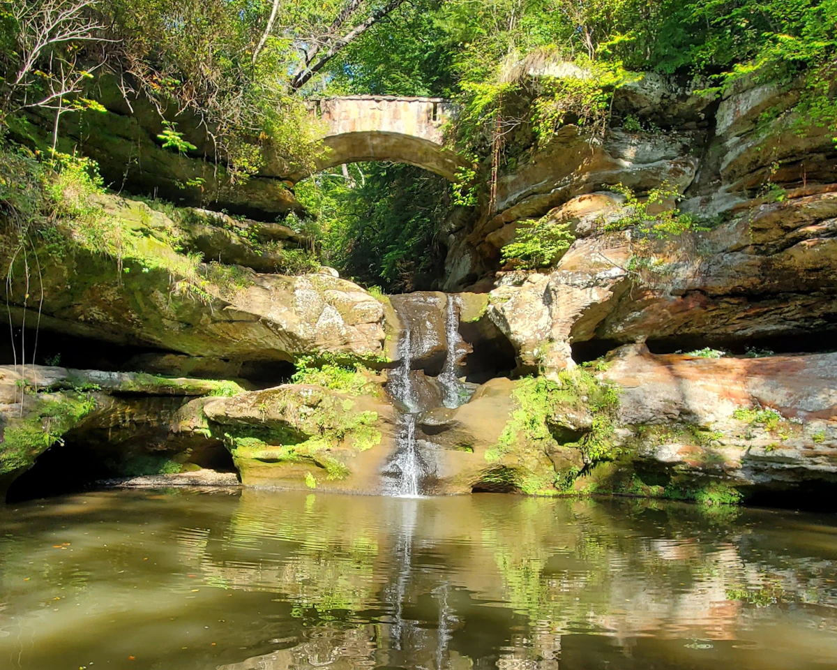 Waterfall falling into a sandstone gorge with a stone bridge above it