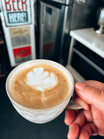 A smiling customer holding a beautifully crafted latte with foam art in a bright kitchen setting.