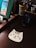 A brown wooden surface holds a cat-shaped mouse pad with a cartoon face featuring whiskers and stripes. Nearby, a desk organizer contains pencils, art supplies, and a cup with yellow drips. A black Sony speaker is visible, and a book with colorful cartoon inserts rests on a wooden stand.