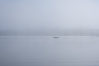 A misty morning on a remote lake, with a lone boat cutting through the calm water.
