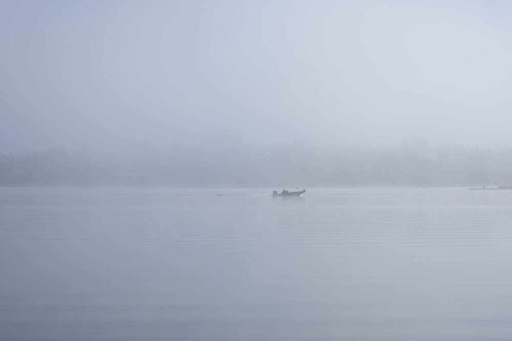 a foggy lake with two boats in the distance