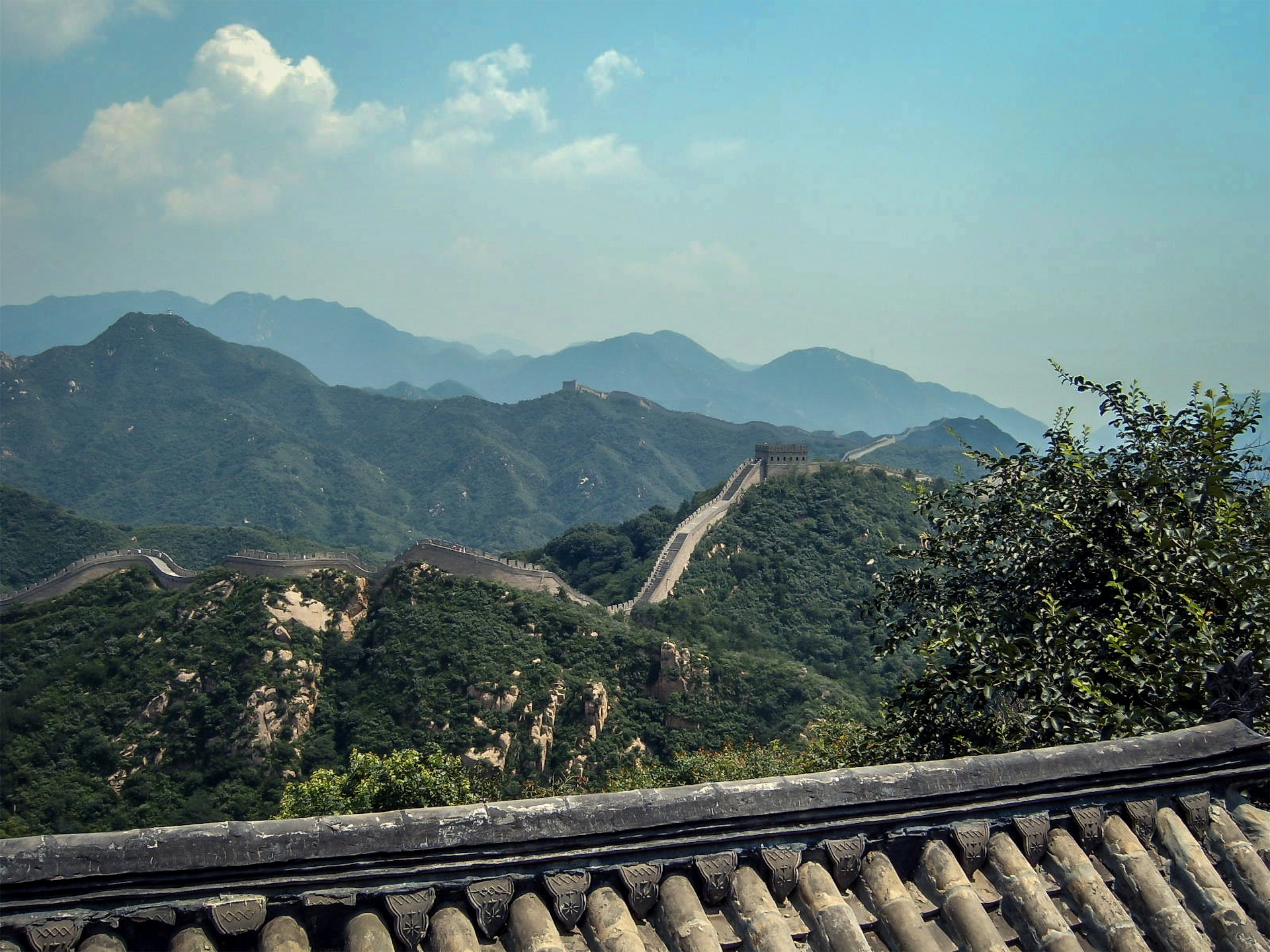 A vibrant photo of the Great Wall of China winding over lush green hills under a clear blue sky.