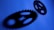 Two interconnected gears are set against a blue background, casting dark shadows that feature distinct shapes and cutouts.