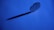 A metal blade stands upright on a blue background, casting a long shadow. The blade has a cross-shaped cutout in the center and curved edges.
