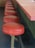 A series of red, round bar stools aligned along a countertop, suggesting a retro or vintage diner style. The stools have metal supports and are positioned on a dark floor, paired with a matching countertop that has a pinkish hue.