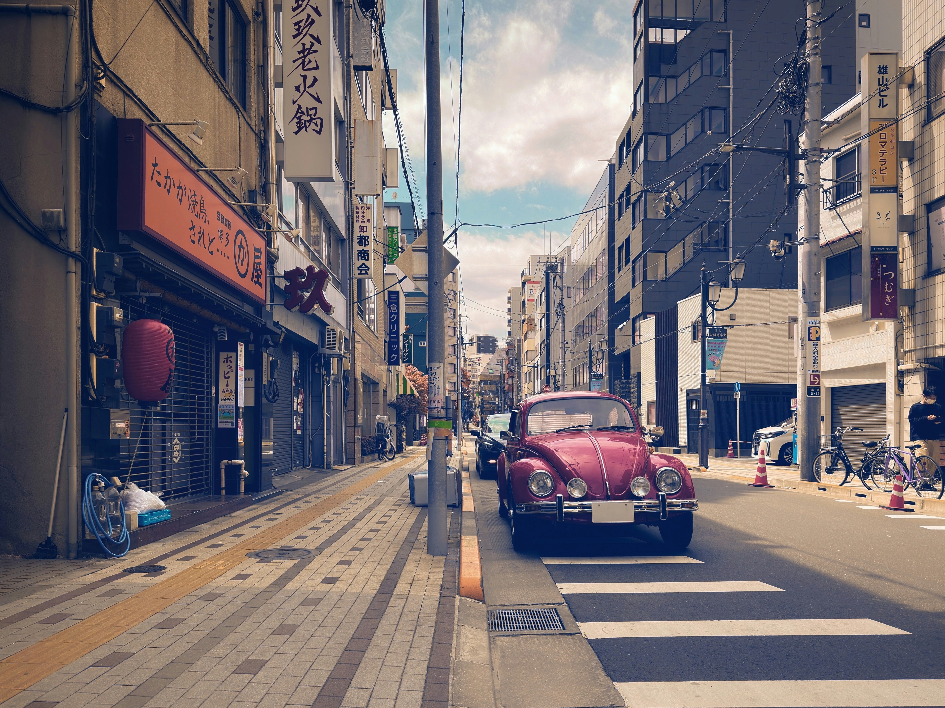 a red car driving down a street next to tall buildings, Red Volkswagen Beetle parked on a backstreet in Yushima, Bunkyo City, Tokyo, Japan.