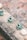 Small ceramic sculptures are displayed on a rough concrete surface. The sculptures are primarily blue-green and appear to depict playful and whimsical creatures or animals, some with detailed patterns or designs. The background is blurred and features earthy tones, creating a rustic outdoor setting.