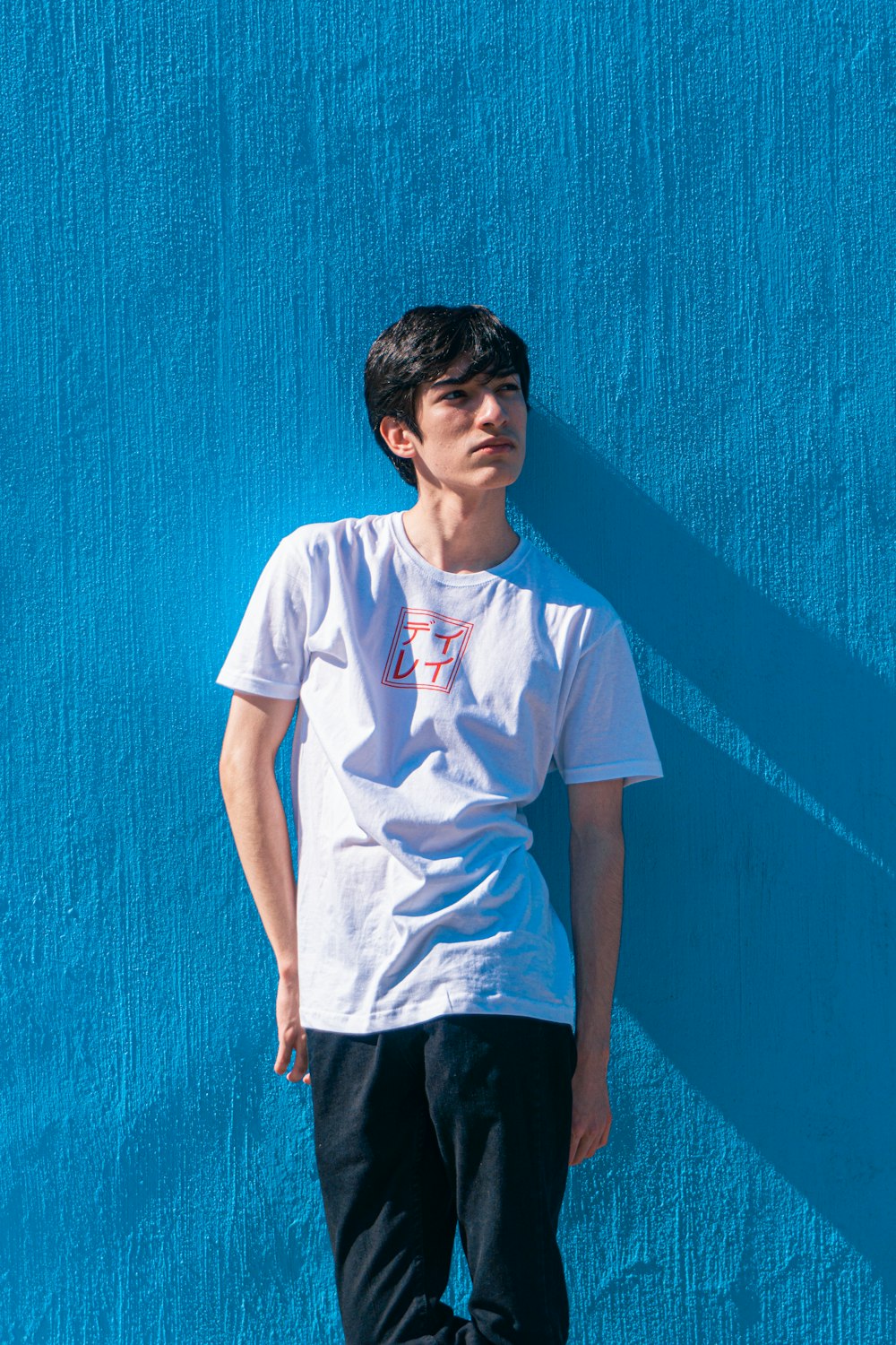 a young man standing against a blue wall