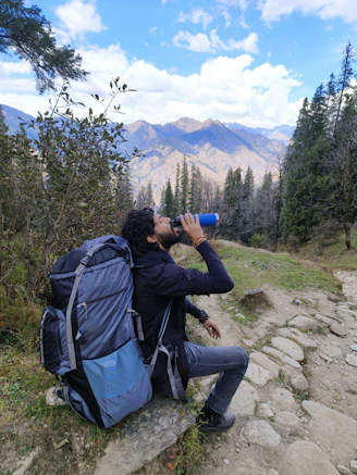 A smiling hiker drinking purified water from a portable bottle on a sunny day.