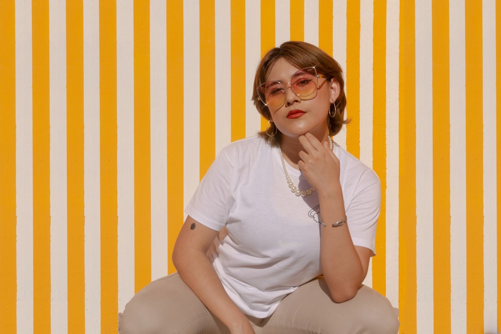 a woman in a white shirt is sitting on a yellow and white striped wall