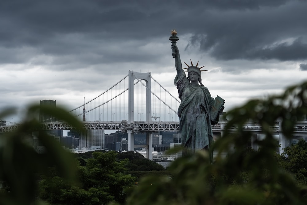 a statue of liberty stands in front of a bridge