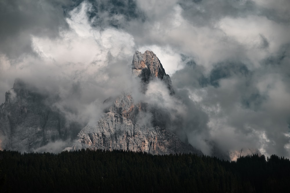 a mountain covered in clouds and trees under a cloudy sky