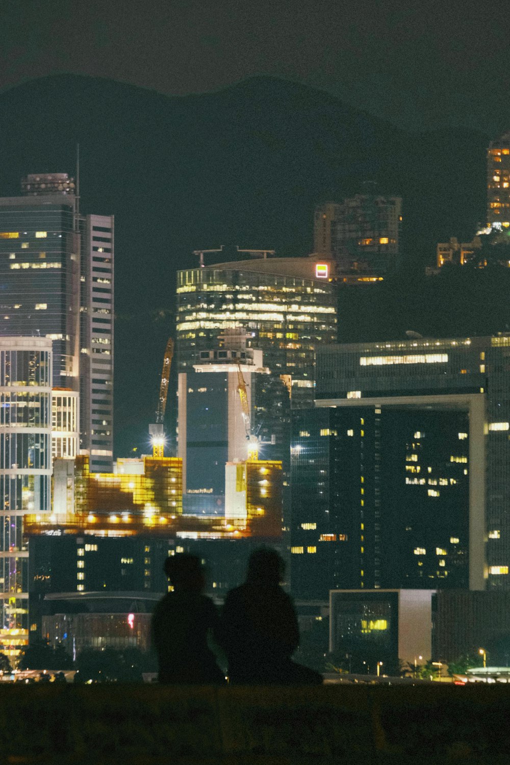 two people sitting on a bench in front of a city at night