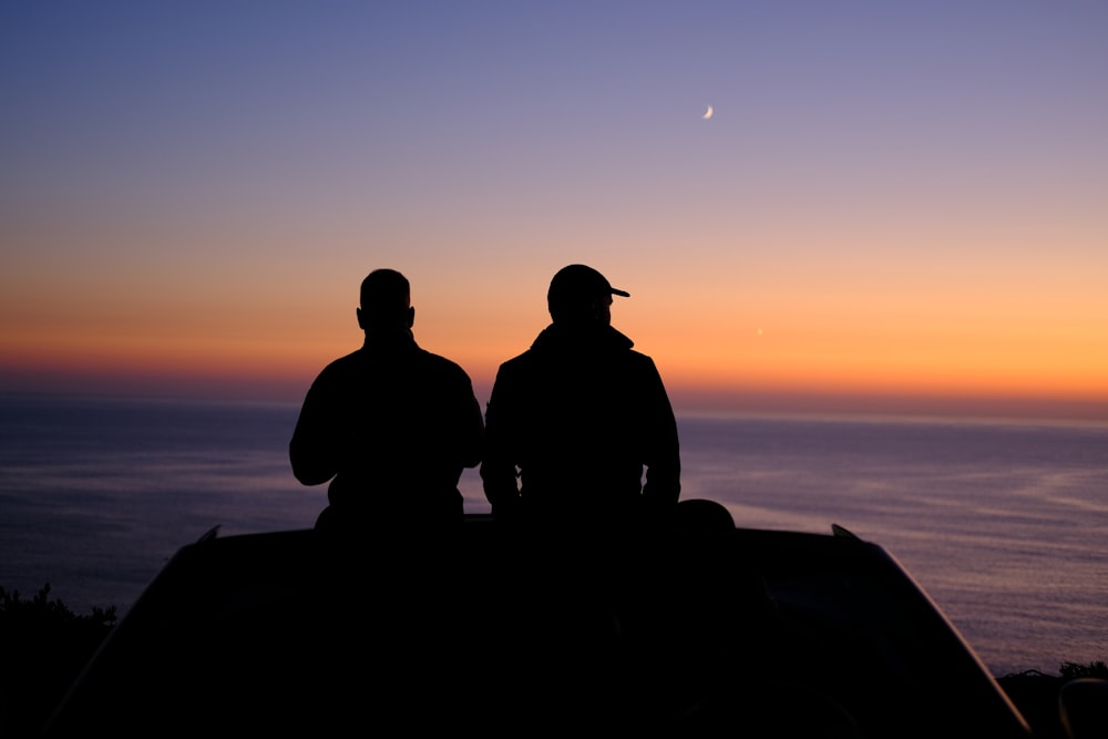 a couple of men sitting on top of a car