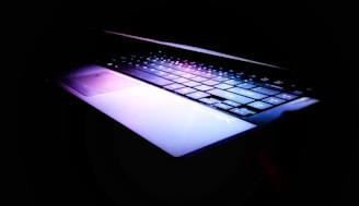 A laptop keyboard illuminated with colorful backlighting in a dark room.