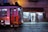 A traditional tram painted in vibrant colors is moving along the cobblestone street in front of a well-lit shop named 'A Pérola da Sé'. The shop has a variety of goods displayed outside, including postcards and souvenirs, and a person can be seen browsing inside.