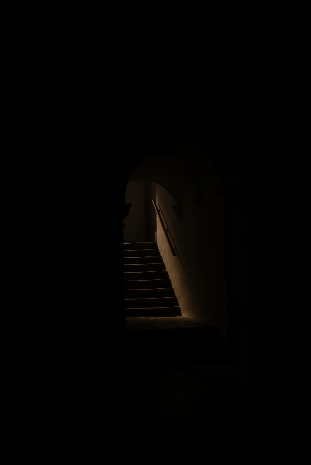 a dark hallway with stairs and a light at the end