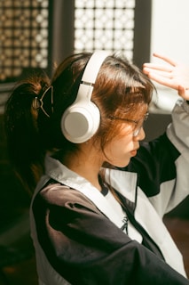 A joyful person listening to music on headphones, smiling with eyes closed in a sunlit room.