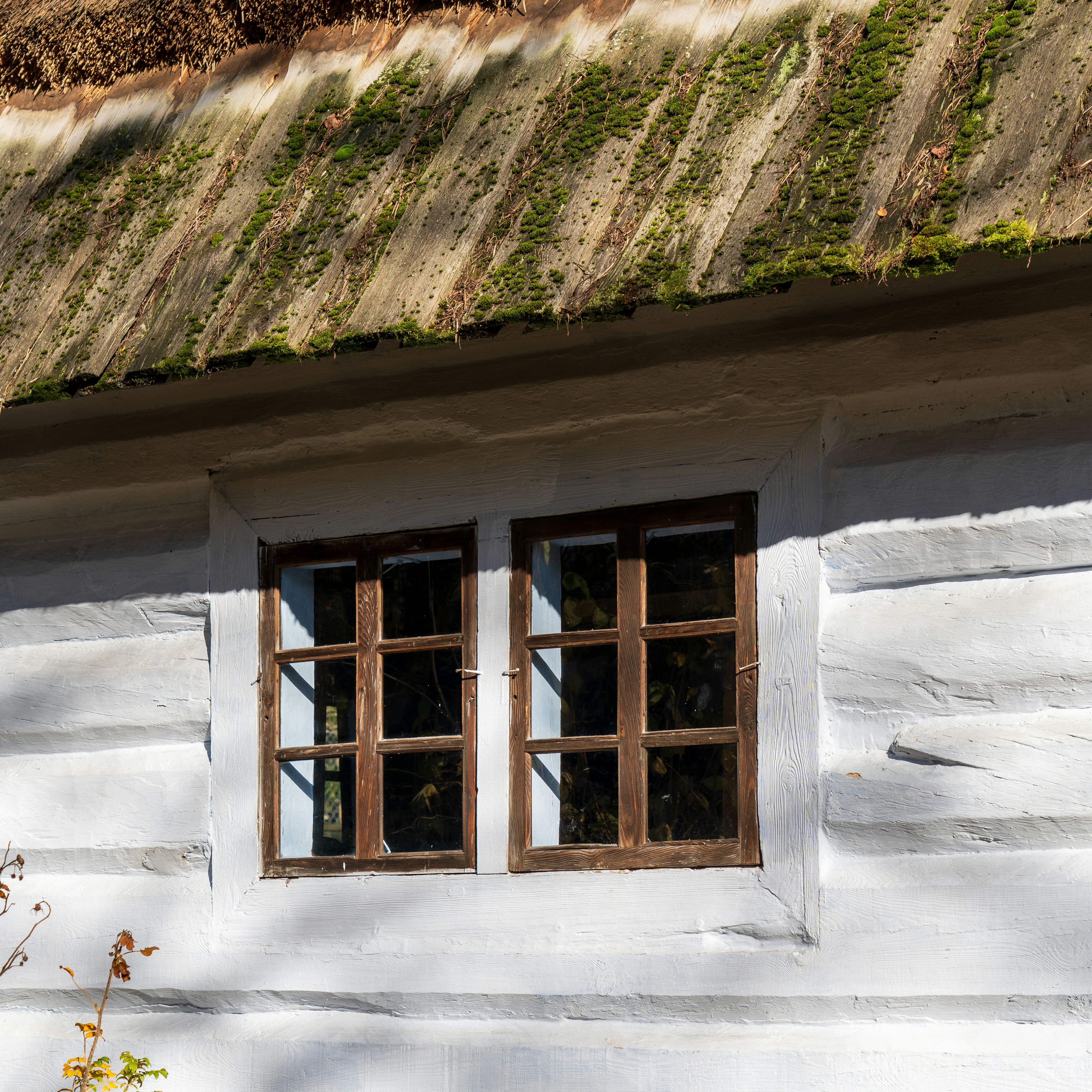 a white building with two windows and a green roof