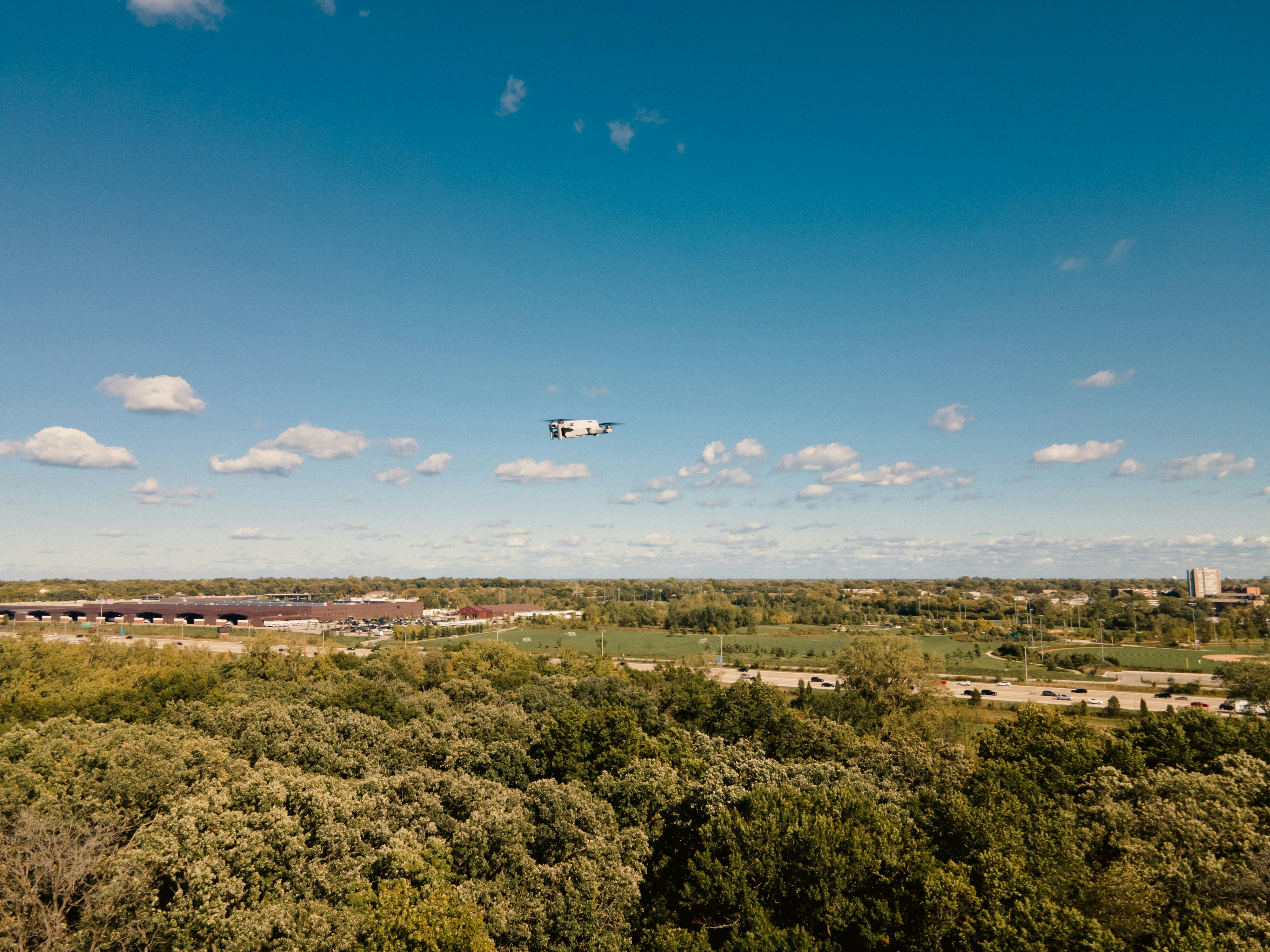 A plane flying over a lush green forest under a blue sky photo – Free ...