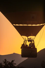 Passengers smiling inside a hot air balloon basket with alpine scenery behind.