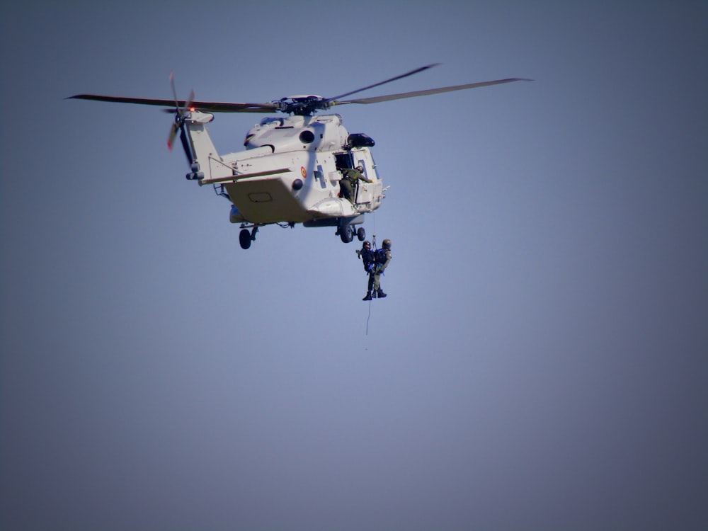 a helicopter is flying in the air with a man hanging from it's side