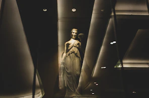 Dramatic black-and-white sculpture bathed in soft golden light against dark brown backdrop.