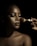 A close-up portrait of a person with flawless makeup, featuring glossy lips and well-defined eyebrows. A hand is applying makeup with a brush, highlighting the contours of the face. The lighting creates dramatic shadows, enhancing the details and texture of the skin.