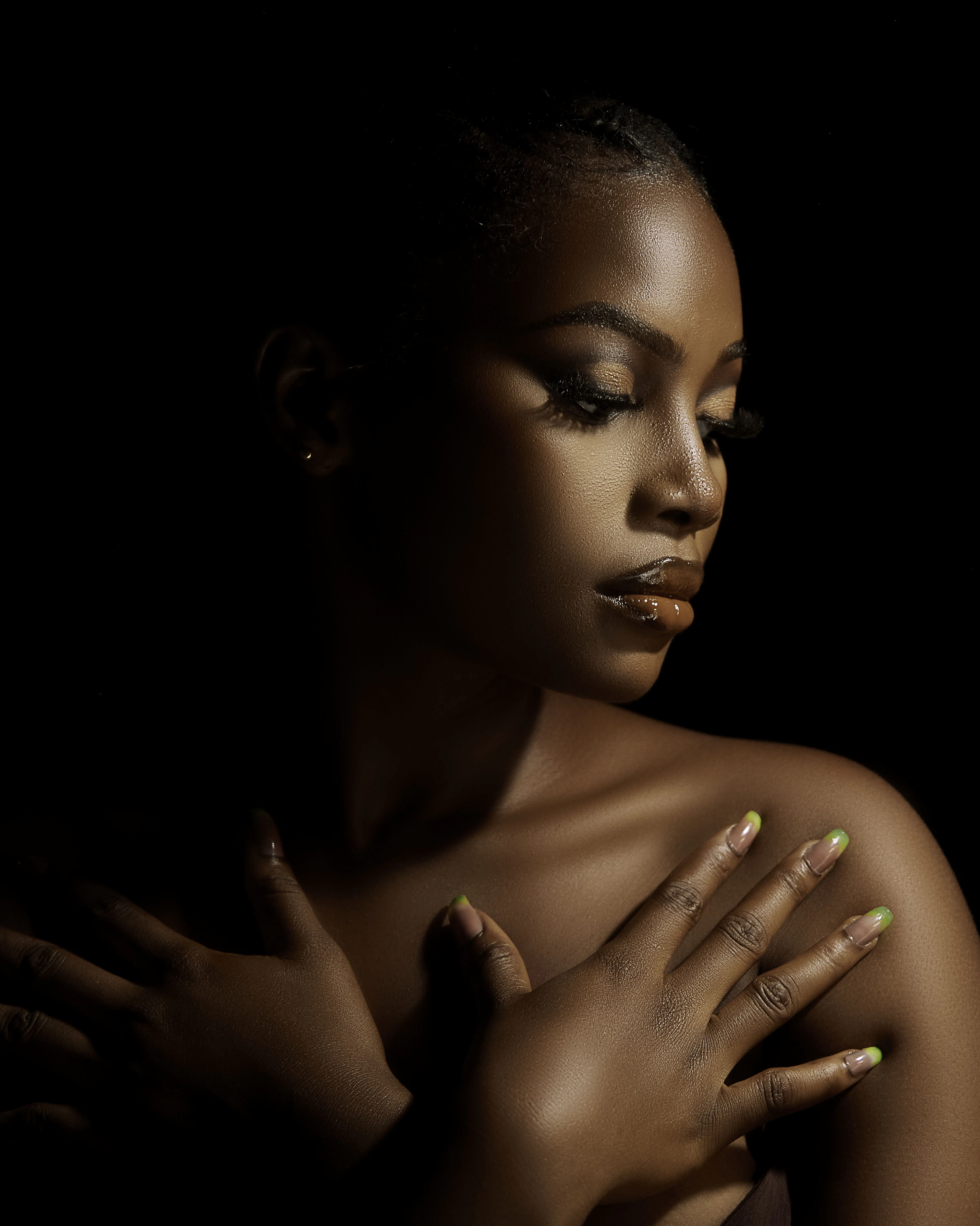Portrait of a woman in low, warm light with her hands resting at her collarbone