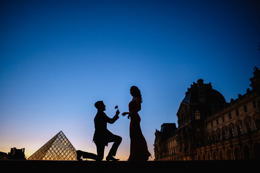 a man kneeling down next to a woman in front of a pyramid