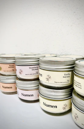 Small jars of creamy body balms and butters arranged on a wooden surface with fresh herbs