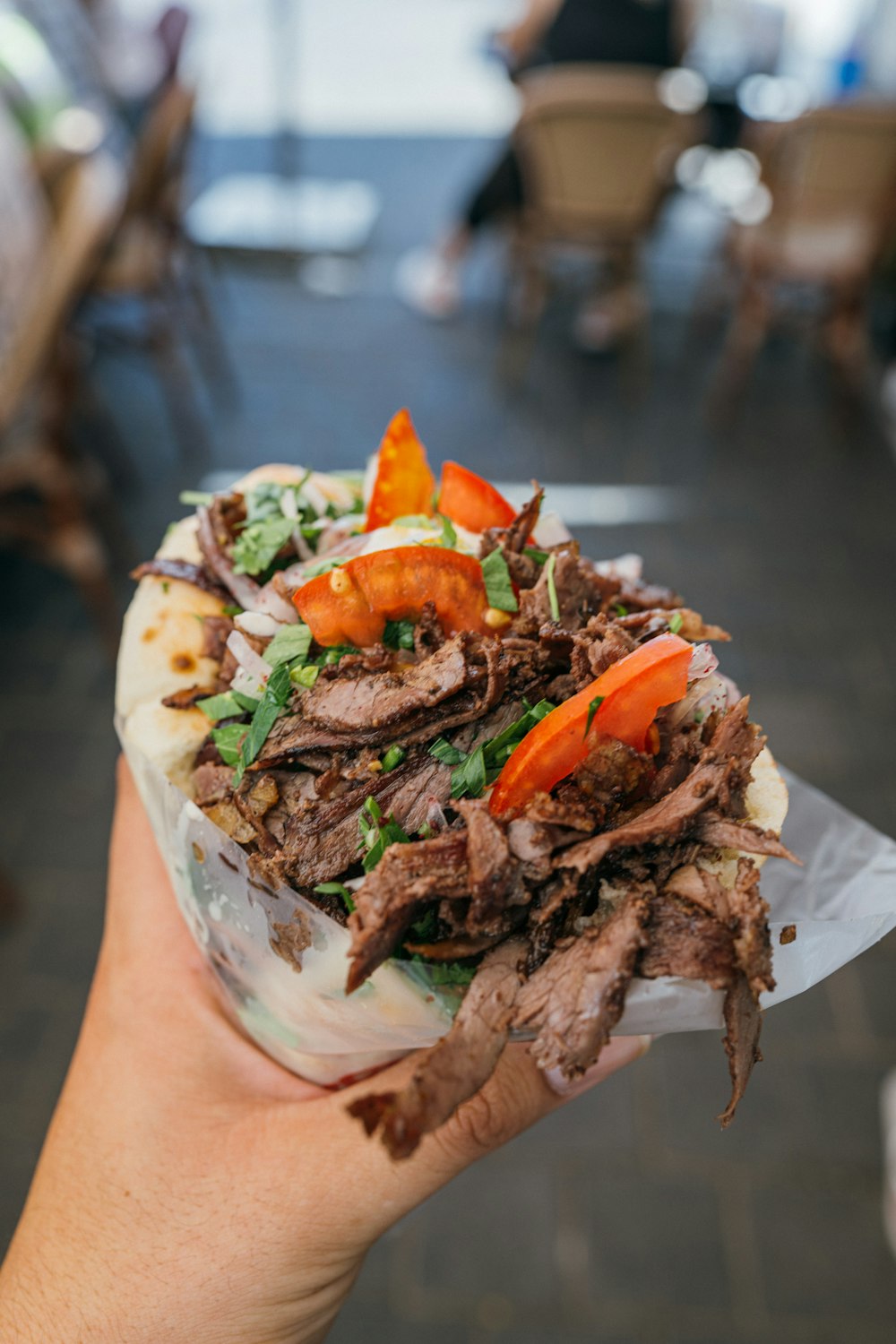 a person holding a sandwich with meat and vegetables