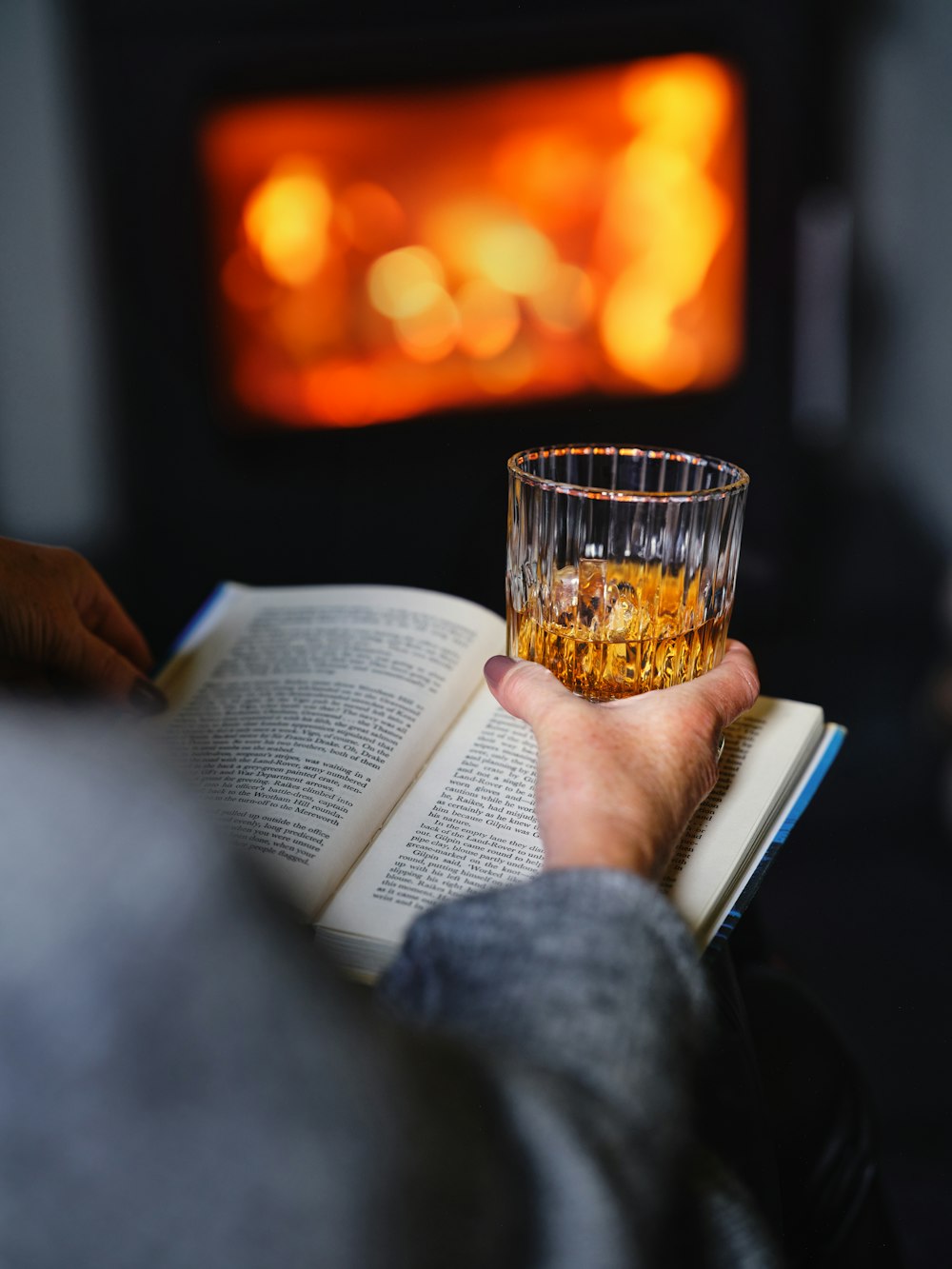 a person reading a book and drinking a glass of whiskey