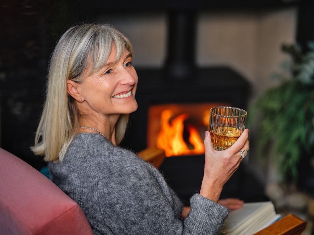 una mujer sosteniendo una copa de vino frente a una chimenea