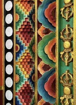 A vibrant and intricate design features geometric and floral patterns in a relief style with various colors and gold accents. The composition includes a series of repetitive designs with circular white dots on a black background, multicolored zigzag patterns, and ornate floral motifs with a gold outline. Deep reds, blues, greens, and oranges dominate the artwork, creating a rich and artistic impression.