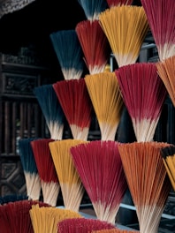 Bundles of incense sticks in various colors including red, orange, and blue are arranged in a visually striking and organized manner. The background is slightly blurred, emphasizing the vibrant colors of the incense sticks.
