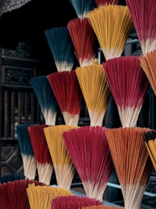 Bundles of incense sticks in various colors including red, orange, and blue are arranged in a visually striking and organized manner. The background is slightly blurred, emphasizing the vibrant colors of the incense sticks.