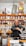 A man is packaging goods in a shop filled with shelves of various spices and herbs stored in jars and bags. The shelves are neatly organized, displaying an array of colorful containers. The man appears to be focused on his task, standing behind a counter with a digital scale.
