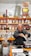 A man is packaging goods in a shop filled with shelves of various spices and herbs stored in jars and bags. The shelves are neatly organized, displaying an array of colorful containers. The man appears to be focused on his task, standing behind a counter with a digital scale.