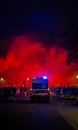 A sleek ambulance with flashing red and blue lights parked at an event entrance during sunset.