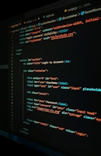 A close-up view of a computer screen displaying HTML and CSS code for a login form. The code includes elements like head, body, various input fields for username and password, and linked style sheets. The text is primarily in blue, white, orange, and green, set against a dark background.