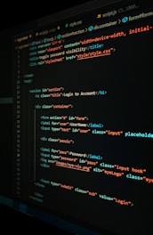 A close-up view of a computer screen displaying HTML and CSS code for a login form. The code includes elements like head, body, various input fields for username and password, and linked style sheets. The text is primarily in blue, white, orange, and green, set against a dark background.