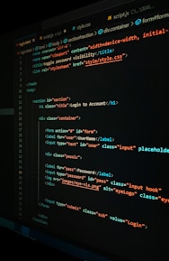 A close-up view of a computer screen displaying HTML and CSS code for a login form. The code includes elements like head, body, various input fields for username and password, and linked style sheets. The text is primarily in blue, white, orange, and green, set against a dark background.